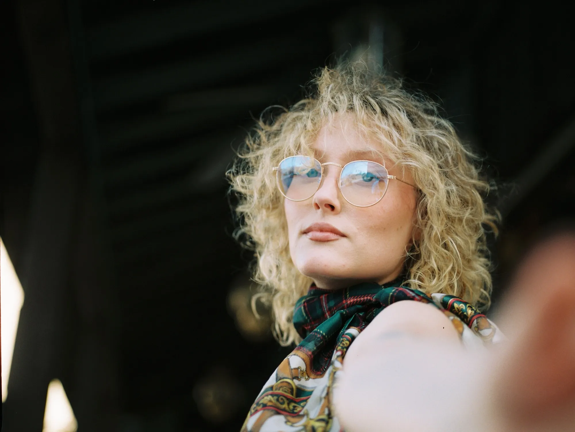 Portrait of L.A.Z.I.E looking past the camera, curly hair and round glasses catching the light